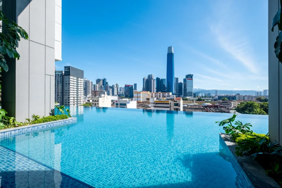 Exterior type: high-rise condominium; features: infinity pool, pool deck with loungers, city skyline view, surrounded by greenery, glass curtain wall facade, tropical landscaping; style: modern.